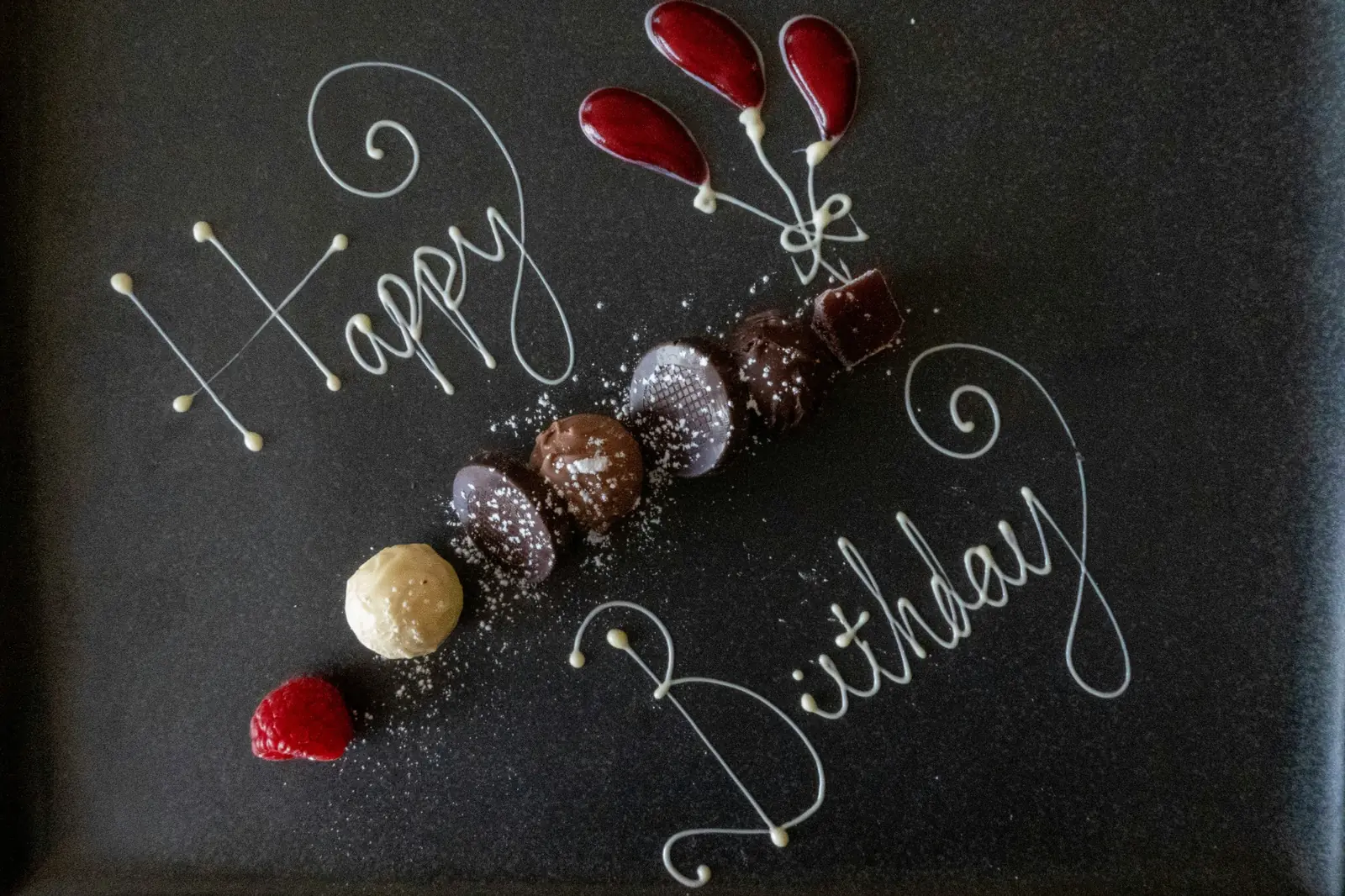 Happy-Birthday-Schriftzug mit Pralinen und roten Ballons